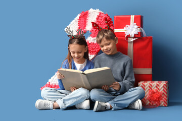 Naklejka premium Cute little children with Christmas gifts reading book on blue background