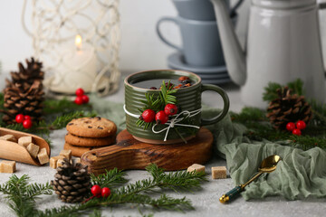 Wooden board with mug of tasty rose hip tea, cookies, forest bumps and fir branches on grey...