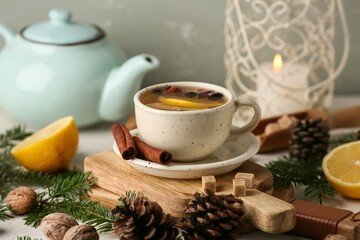 Winter composition with mug of tasty rose hip tea, lemons, teapot and fir branches on white table near grey wall