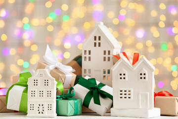 Winter composition with decorative houses and Christmas gift boxes on white table against blurred...
