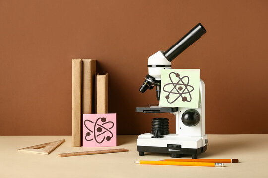Microscope with drawn molecules, books and stationery on beige table against brown background. Nobel Prize Day - Powered by Adobe