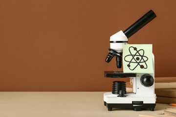 Microscope with drawn molecule and books on beige table against brown background. Nobel Prize Day