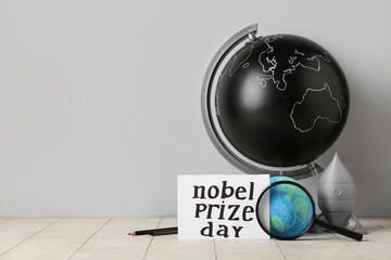 Paper with text NOBEL PRIZE DAY, globe, rocket and magnifier on tile against grey background