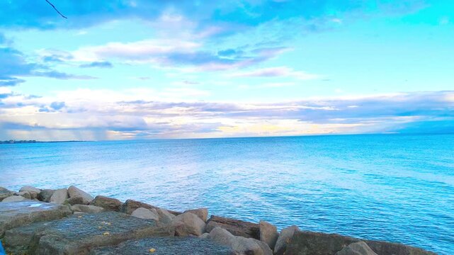 Gentle ocean waves lapping against rocky shoreline under a bright cloudy sky, perfect for travel videos, serene nature scenes, or peaceful coastal backgrounds, bringing a sense of calm and natural bea