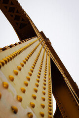 Obraz premium Unique View of Golden Bridge Structure With Detailed Rivets Against a Cloudy Sky