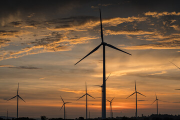 Obraz premium Electricity generating station, Wind turbines power generator in agricultural fields at sunset, Alternative Energy Windmill Farm, Clean energy concept.