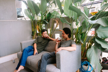 Obraz premium Two Friends Relaxing and Enjoying Drinks on a Modern Sofa