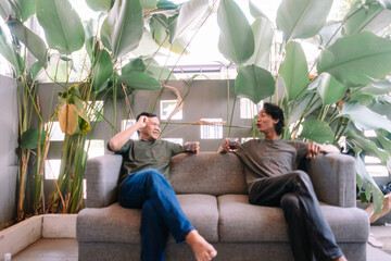 Happy Male Friends Chatting and Relaxing on Sofa Surrounded by Plants