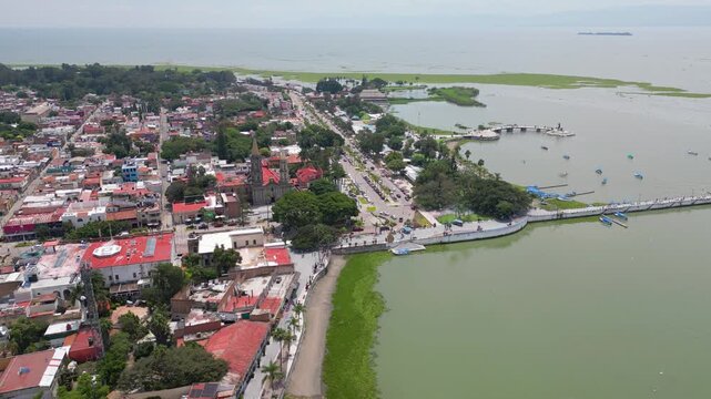 Drone's high-angle perspective of Chapala, Mexico, reveals its charming town, busy malecon boardwalk, and Lake Chapala, featuring a historic church and boats.