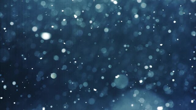 Gentle snowflakes dance in slow motion on dark blue background with bokeh