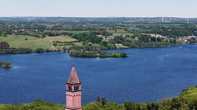 Drone footage capturing the Himmelbjerget sky mountain tower next to a deep blue lake in Denmark.