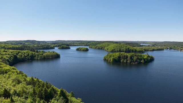 Aerial footage of a deep blue lake or sea with small green islands in Denmark captured by drone. The camera pans over open water and lush tree-covered islands under a clear sky.