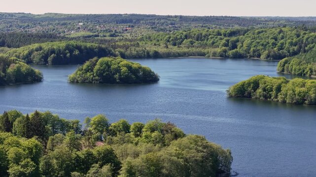 Aerial footage capturing a blue lake with tree-covered islands and surrounding green forests and countryside near Aarhus Bay in Denmark. The drone pans across the tranquil water and scenic landscape.