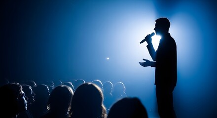 Man speaking into microphone on stage with audience in blue light