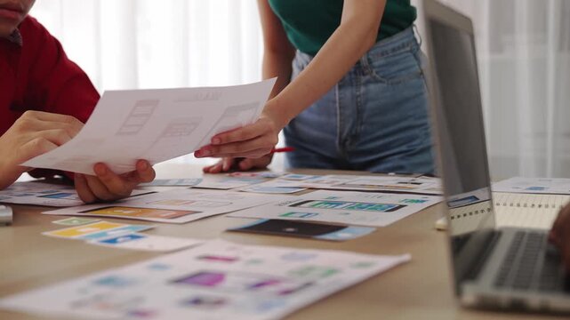 Excellent startup company employee presenting user interface prototype for mobile application to smart co-worker in office workspace. UX UI designer praising function of icon design on paper. Synergic