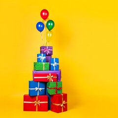 Colorful gifts stacked with balloons against a vibrant yellow background for celebrations