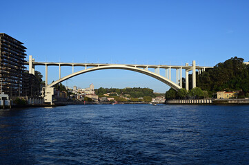Arrabida Bridge over Douro River in Porto, Portugal in afternoon light under clear skies.