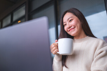 Portrait image of a woman drinking coffee while working on laptop computer in cafe