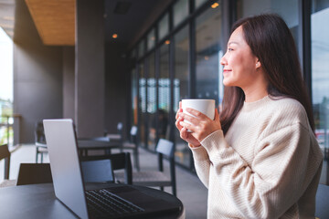 Portrait image of a woman drinking coffee while working on laptop computer in cafe