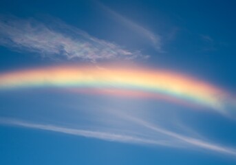 Vibrant rainbow arc across bright blue sky with wispy clouds and sunlight