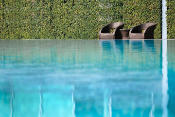 Relaxing Poolside Wicker Chairs with Green Hedge and Water Reflection