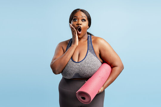 Excited African American plus size model wearing stylish top holding yoga mat looking at camera