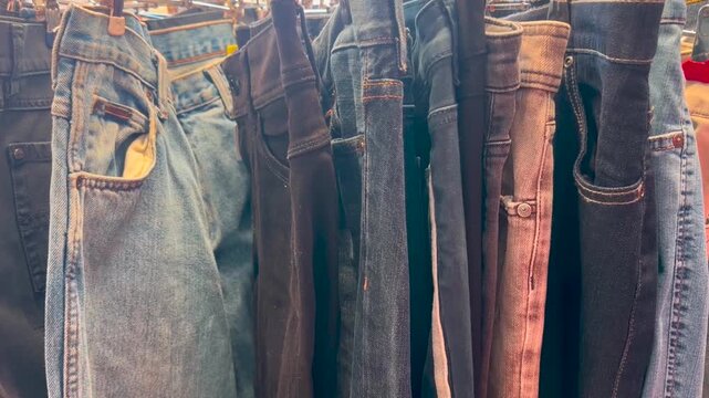 Jeans in various colors hang on a clothes rack in a secondhand store. zooming in