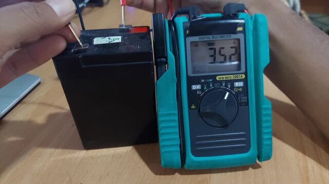 Close-up shot of checking the voltage of a weakened emergency lamp battery using a digital multimeter, showing detailed measurement and troubleshooting process.
