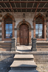 Entrance of Kayseri Clock Tower, Saat Kulesi, in Kayseri, Turkey. Features an ornate arched wooden door, stone facade, arched windows, and a balustrade.
