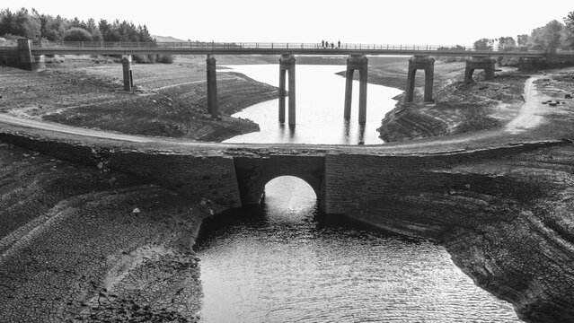 Aerial monotone view of a drained reservoir with exposed bridge and low water channel