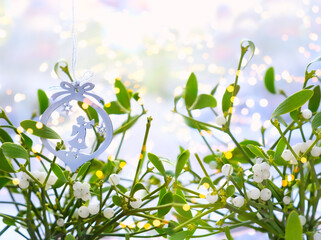 Fototapeta premium Mistletoe green branches and christmas decor with angel on light abstract background. Tradition decoration for Christmas holidays, festive winter season. Christmas plant mistletoe (Viscum album)
