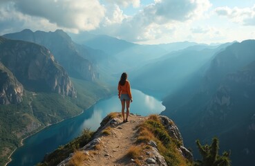 Woman hiker on mountain peak. She looks at blue lake and misty valleys from high cliff. Person enjoys scenic nature view during summer hike.