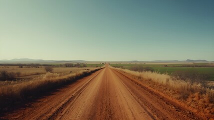 Naklejka premium A wide open countryside scene featuring a long reddish-brown dirt road stretching into the distance