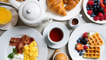 An Overhead View of a Lavish Breakfast Spread Featuring Croissants, Berries, Waffles, Bacon, Eggs, and Tea, Perfect for a Delicious Morning Meal