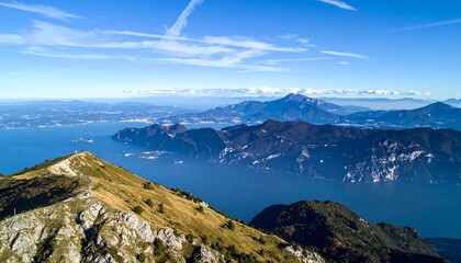 A mountain peak overlooks a scenic lake surrounded by hills under a blue sky with clouds