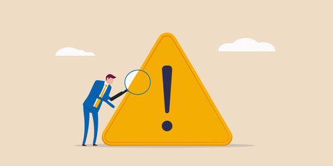 Businessman inspecting warning sign with magnifying glass risk management concept