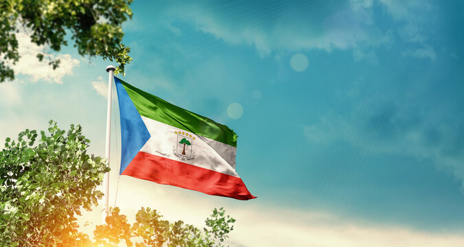 Equatorial Guinea national flag waving in the sky behind the tree. The flag blowing with beautiful sunlight. Equatorial Guinea national flag for independence day.