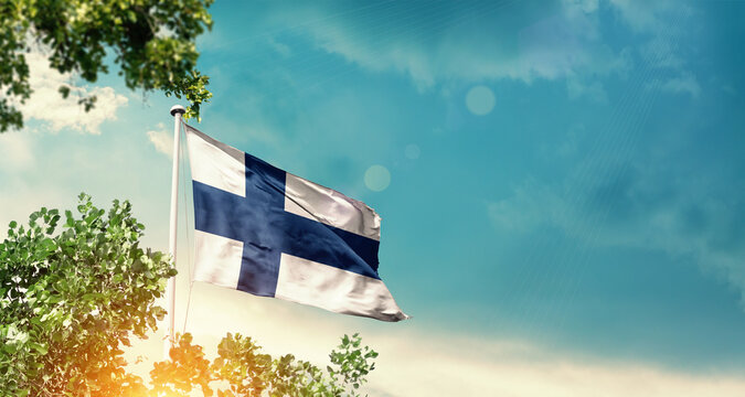 Finland national flag waving in the sky behind the tree. The flag blowing with beautiful sunlight. Finland national flag for independence day.