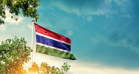 The Gambia national flag waving in the sky behind the tree. The flag blowing with beautiful sunlight. The Gambia national flag for independence day.