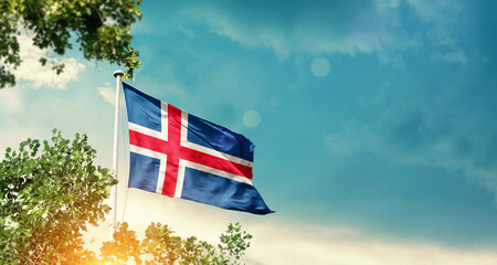 Iceland national flag waving in the sky behind the tree. The flag blowing with beautiful sunlight. Iceland national flag for independence day.