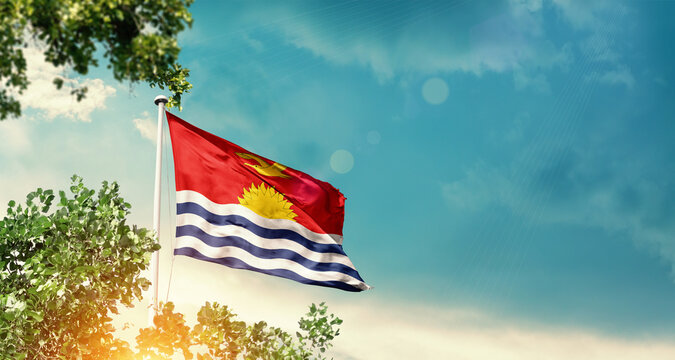 Kiribati national flag waving in the sky behind the tree. The flag blowing with beautiful sunlight. Kiribati national flag for independence day. - Powered by Adobe