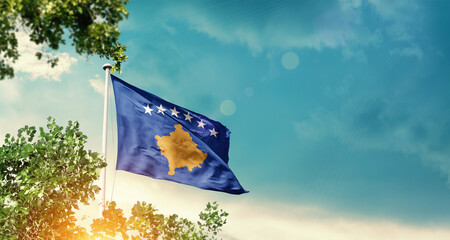 Kosovo national flag waving in the sky behind the tree. The flag blowing with beautiful sunlight. Kosovo national flag for independence day.