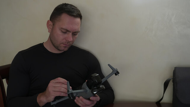 A man repairs drones at home. Working on quadcopters. A man in a black T-shirt at work.