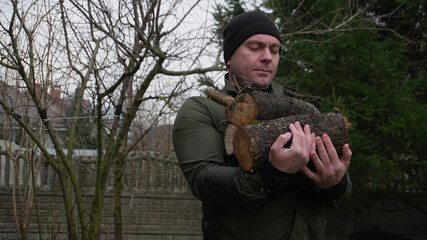 A man works at home, a man works in the garden, daily chores around the house. A man carries chopped logs in his hands.