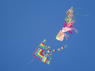Series of colorful kites flying over a sunny beach in Italy, arranged in a different pattern against a clear blue sky during a bright summer day.