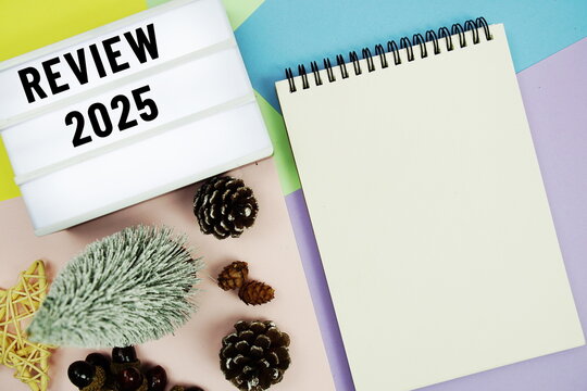 Review 2025 text in lightbox with notepad and Christmas tree and pine cone decoration on mix color pastel background