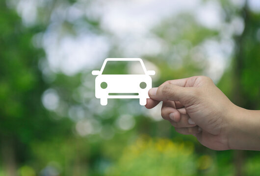 Hand holding car flat icon in fingers over blur green tree in park, Business transportation service concept