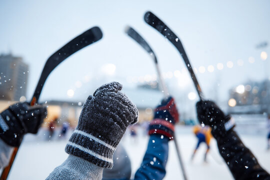 Faceless young adults celebrating a goal on an outdoor rink, emphasis on raised sticks and snowy air particles, players intentionally defocused, with copy space