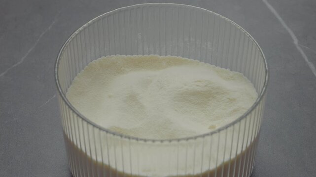 Hands carefully open a container filled with powdered milk. This process shows how simple and convenient it is to access milk powder for various uses.
