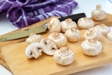 Whole and sliced button mushrooms on a rustic wooden cutting board with a chef's knife. Preparation shot for cooking, recipe, and culinary concepts, viewed from above.
